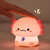 Cute cartoon-style night light with a hand touching it, glowing warmly on a soft brown background.