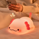 Cute axolotl-shaped night light on a soft surface with a person using a phone in the background.