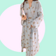 Long sleeve light blue robe with teddy bear pattern held by a person against a pink background. The robe is made of textured cotton 