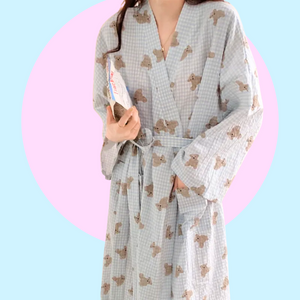 Long sleeve light blue robe with teddy bear pattern held by a person against a pink background. The robe is made of textured cotton 