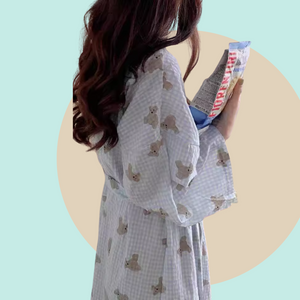 Long sleeve light blue robe with teddy bear pattern held by a person against a pink background. The robe is made of textured cotton 