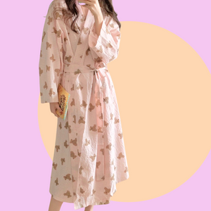 Long sleeve pink robe with teddy bear pattern held by a person against a pink background. The robe is made of textured cotton 