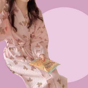 Long sleeve pink robe with teddy bear pattern held by a person against a pink background. The robe is made of textured cotton 