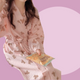 Long sleeve pink robe with teddy bear pattern held by a person against a pink background. The robe is made of textured cotton 