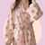 Long sleeve pink robe with teddy bear pattern held by a person against a pink background. The robe is made of textured cotton 