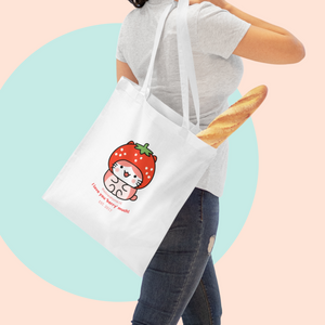 Person holding a white tote bag with a cute design of a strawberrry Ichigo kitty designed by The Linea Home, the slogan says ' I love you berry much'