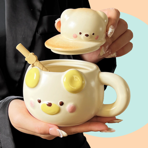 Cute ceramic mug with a lid shaped like a bear. The mug is in a butter cream colour, and has a short straw on the side. 