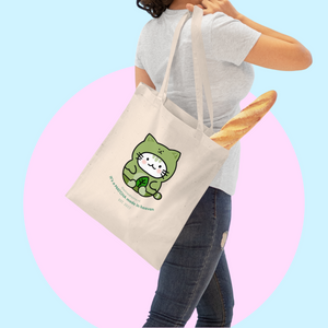 Person holding a tote bag with a green cat illustration against a colorful background