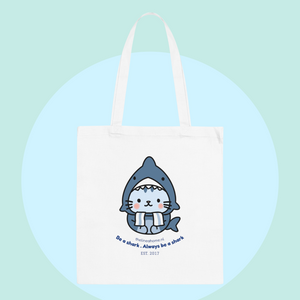 White tote bag with cute shark kitty illustration, blue text, and green sneakers, ideal for adding playful style to shopping. Tote bag