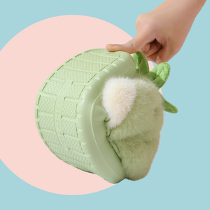 Green plushy slippers that looks like strawberries finished in green plushy leafy stalk and seeds detail. The slipper is turned upright with a hand squishing it, the slipper is bent to show how soft and flexible it is. 